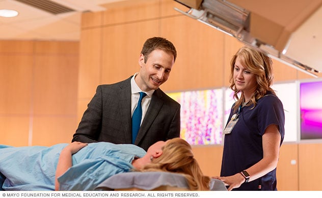 Proton beam specialists conferring with a patient in a treatment room.